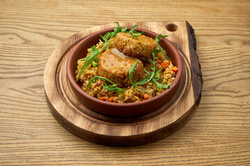 Vegetarian dish of chickpea cutlets in mustard sauce with bulgur in a clay bowl on a wooden background.