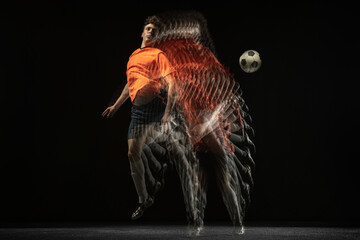 Young caucasian football soccer player in motion and action in mixed light on dark background.
