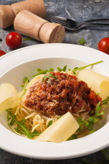 spaghetti Bolognese on a white plate with Parmesan and arugula. Vertical frame