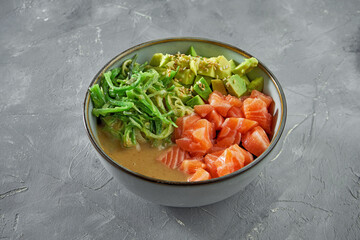 Traditional japanese dish - poke bowl with salmon, wakame, avocado and peanut sauce on a gray background. Healthy superfood