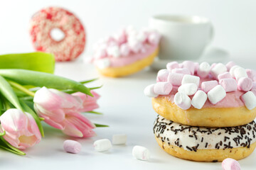 Obraz na płótnie Canvas Sweet donuts with marshmallows and tulips flowers, on a white background, scattered marshmallows, close-up view from the front