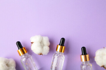 Serum or oil bottle with pipette and cotton twig on purple background with copy space. Beauty...