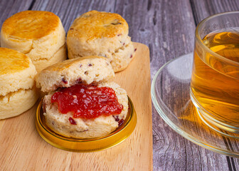 Scones traditional English delicious freshly baked homemade with strawberry jam placed on a wooden tray and a teacup on a wooden table. Close-up photo. Dessert, beverage, and relaxation concept