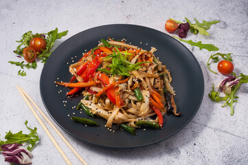 Udon noodles with vegetables on a black plate. Asian cuisine