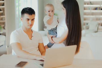 Young father works on laptop while his wife looks after child.