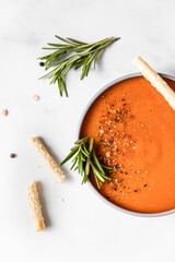 Tomato soup garnish with ground pepper, rosemary and bread sticks, light background. Top view.