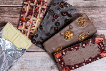 Different kinds fof chocolate bars on vintage wooden background. Dark one, milk and white, with pieces of nuts, fruits and berries. Craft homemade sweeties. Copy spce.