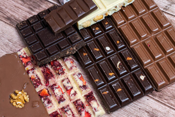 Different kinds fof chocolate bars on vintage wooden background. Dark one, milk and white, with pieces of nuts, fruits and berries. Craft homemade sweeties. Copy spce.