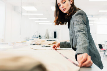 Female fashion designer measures the fabric. Young woman business owner working with a garment for a new collection in her creative office.