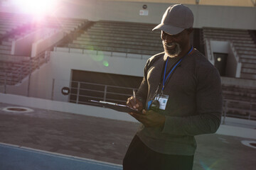 African american male coach with clipboard taking notes on running track in the stadium