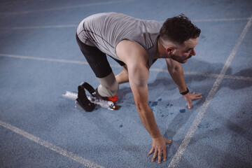 Caucasian male athlete with prosthetic leg in starting position for running on the track at night