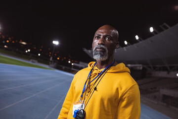 African american senior male coach standing on the running track at night