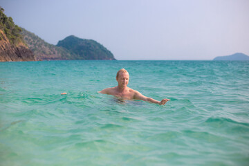 An adult European man swims in the azure sea water on a tropical island. Travel and tourism on summer vacation days