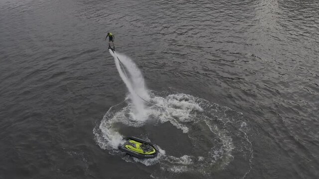 A man flies over the river on a flyboard and dives into the water. Flyboarding is a new extreme water sport. a man performs tricks in flight. Spectacular sports coups and turns. aerial view