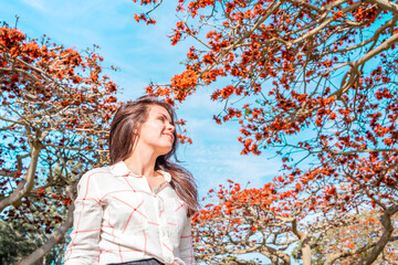 Young brunette girl against the sky and a blooming tree with red flowers, Los Angeles, Calfiornia
