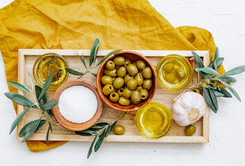 Overhead view of a tray with bowls of olive oil, a bowl of green olives and a bowl of seas salt on a crumpled napkin