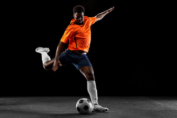Young African football soccer player playing isolated on black background. Concept of sport.