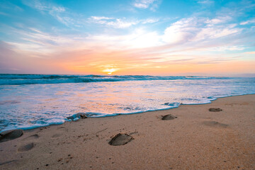 Footprints in the sand in front of the ocean during sunset, calm ocean and beautiful colorful sky, California