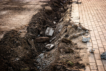 Empty trench along the pedestrian sidewalk. A narrow trench was dug for a curbstone installation....