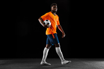 Portrait of young African soccer player posing isolated on black background. Concept of sport.