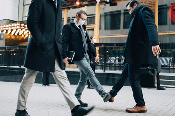 Businessmen greeting with foot tap on footpath in city during pandemic