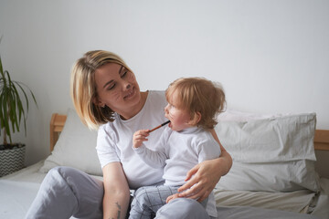 young mom and little son have fun at home on the bed, draw funny faces on their faces