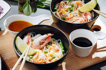romantic dinner for two. Asian cuisine, rice noodles with shrimp and seafood, green peas and onions. soy sauce and various fresh vegetables. romantic dinner in black plates with Japanese chopsticks