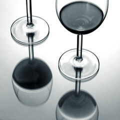 Two wine glasses with red wine mirroring on glass table; minimalist abstract black and white photo.