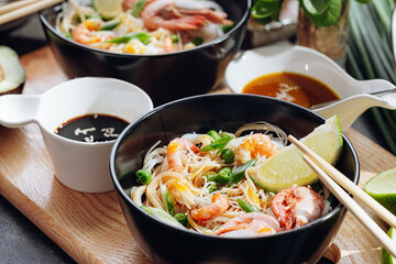 Fototapeta na wymiar romantic dinner for two. Asian cuisine, rice noodles with shrimp and seafood, green peas and onions. soy sauce and various fresh vegetables. romantic dinner in black plates with Japanese chopsticks