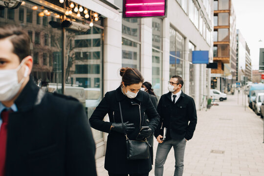 Female entrepreneur holding smart phone while standing in line with colleagues during COVID-19