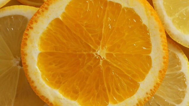 Lemon slices with one cut orange slice closeup, summer background, fruits top view. Rotation
