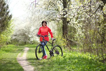 Beautiful woman on a bike in a blooming spring garden. Beautiful mature woman posing for the camera in a blooming spring garden.