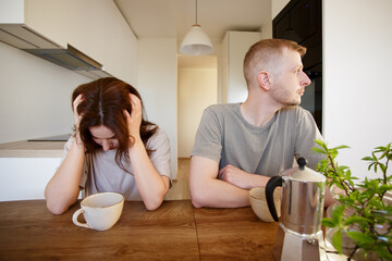 love, quarrel, stress and relationship concept - sad couple sitting in modern kitchen after quarrel