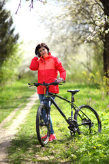 Fototapeta premium Beautiful woman on a bike in a blooming spring garden. Beautiful mature woman posing for the camera in a blooming spring garden.