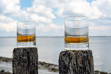 Tasting of dram single malt scotch whisky on seashore in Scotland, old wooden pole with whisky glass