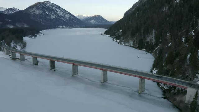 Aerial view, black car driving over beautiful bridge in the alps, lake frozen below.