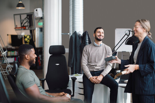 Female and male colleagues laughing while discussing over product at creative office