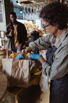 Female entrepreneur packing order in paper bag at delicatessen shop