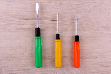 Green, yellow and orange screwdrivers on a wooden background