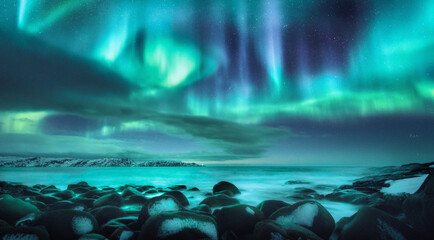 Noorderlicht. Aurora borealis over oceaan in Teriberka, Rusland. Sterrenhemel met poollicht en wolken. Nacht winterlandschap met heldere aurora, sterren, zee, besneeuwde stenen in wazig water. Reis