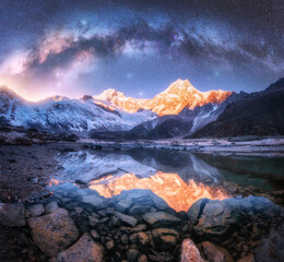 Milky Way over snowy mountains and lake at night. Landscape with snow covered high rocks, starry...