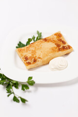 Fried pancake stuffed with sour cream and parsley on a white plate