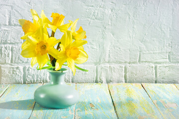 bouquet of fresh yellow daffodil flowers in a vase against a white brick wall background and textured wooden surface