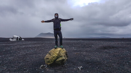 Iceland - Young man standing on a big rock with a plane wreck in the back.