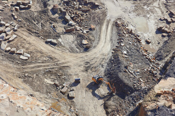 An aerial view taken from a helicopter of an orange excavator in a large stone quarry in Britain. Rock and gravel can be seen around the piece of heavy machinery.
