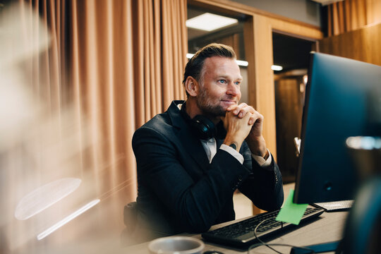 Smiling male entrepreneur with hand on chin working over laptop in office
