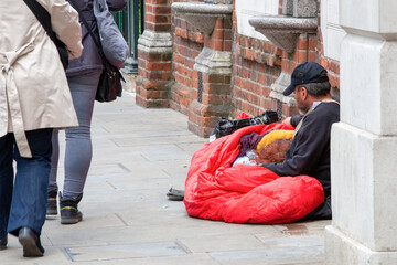 Couple of homeless, beggars lying on the ground against the passing by people.A man holds his woman...