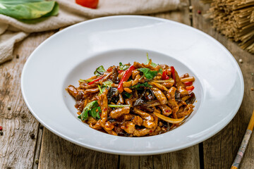 aromatic roast sliced pork with vegetables in hot sauce on old wooden table