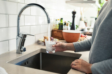 Midsection of woman holding glass under faucet in kitchen