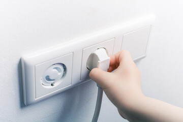 Child Hand Pulling A Power Cord Out Of A Wall Socket With Safety Plugs - Prevent Child Hazard Concept